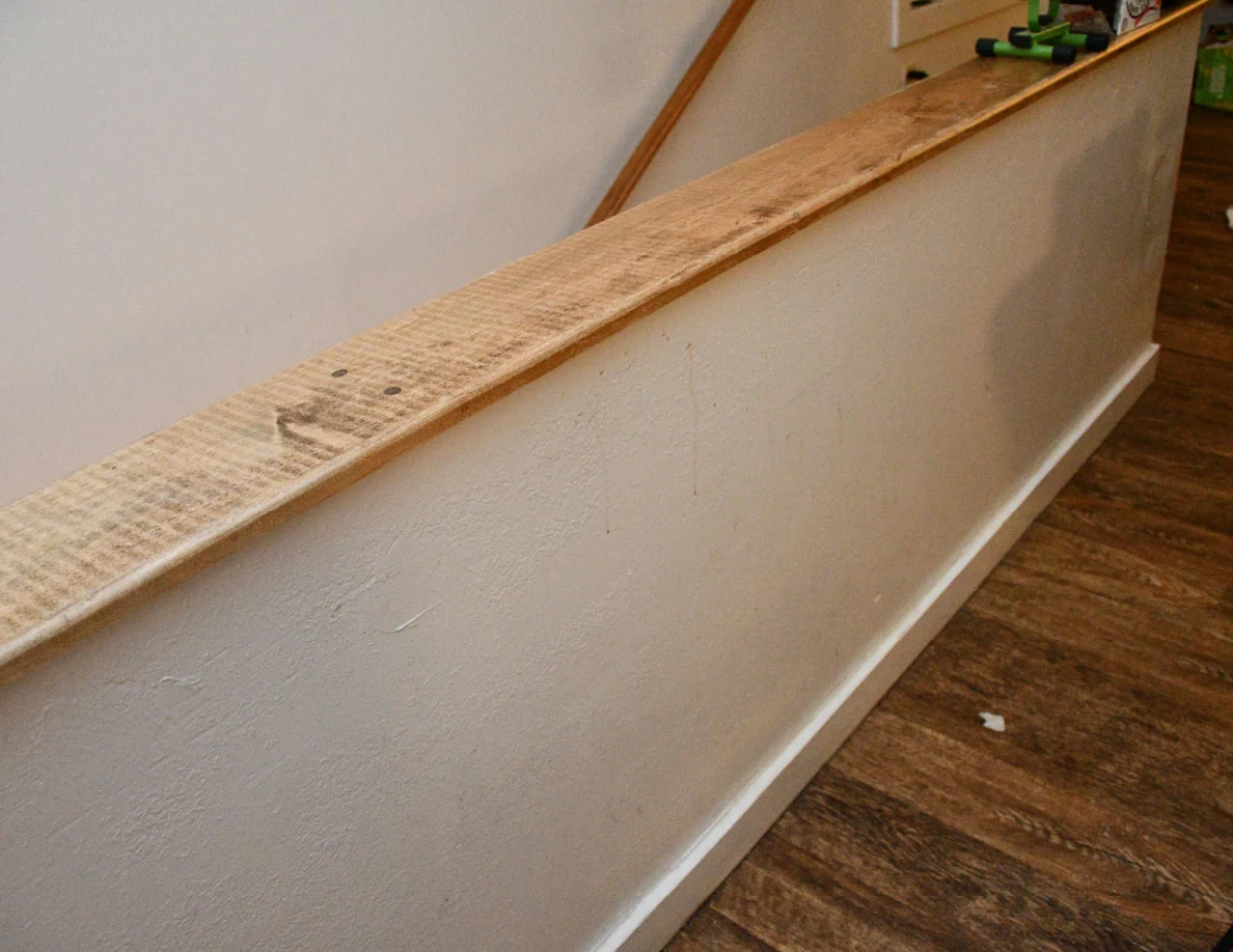 Wood-capped stair half-wall beside wood-look flooring and wooden handrail.