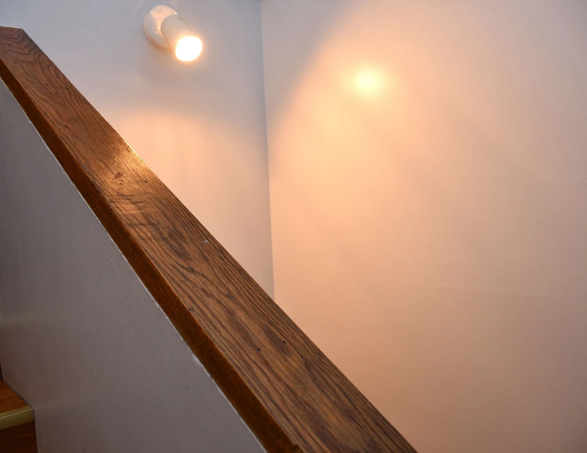 Wooden stair half-wall cap beneath a wall-mounted light.