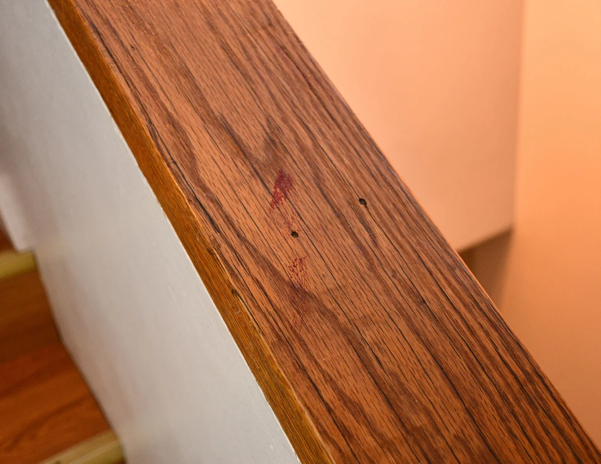 Close view of a reddish mark and small dark spots on a wooden stair rail cap.