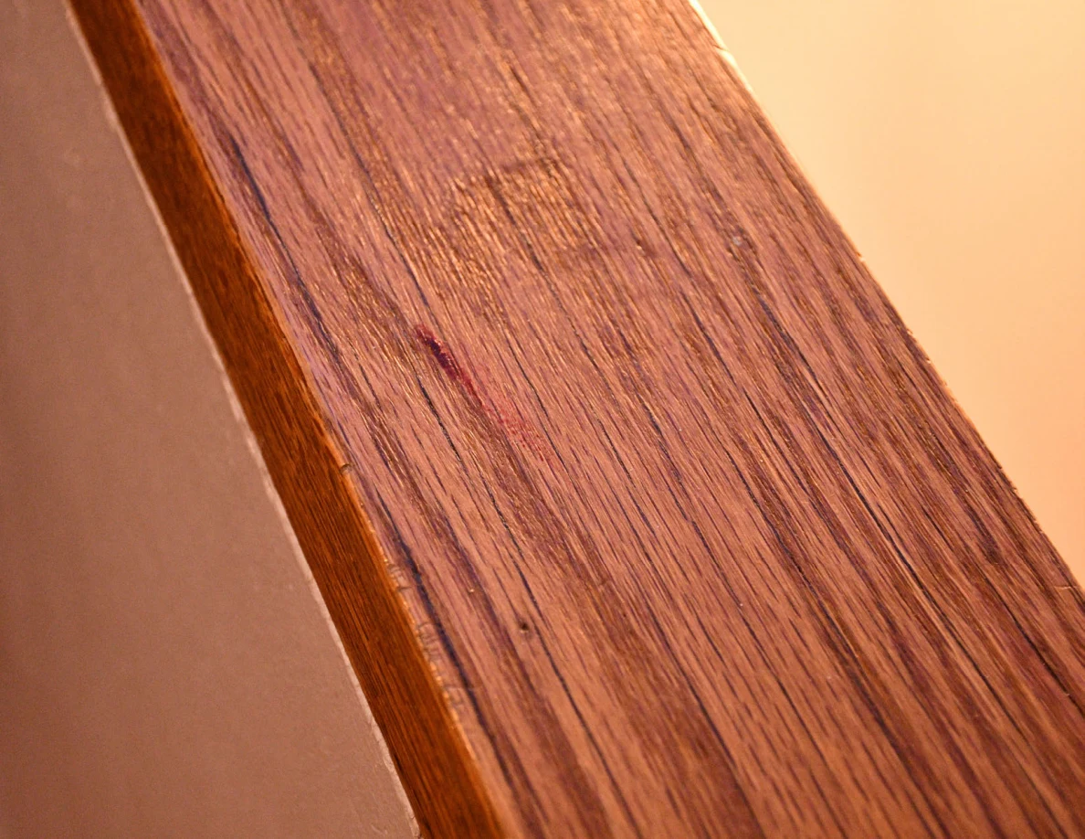 Closer view of a reddish mark on wood-grain stair rail cap.