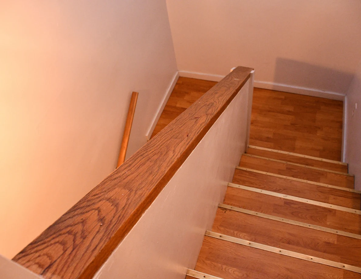 View down wooden stairs beside a wood-capped half-wall and wooden handrail.