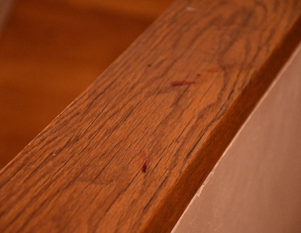 Close view of small reddish marks on a wood-grain stair rail cap.