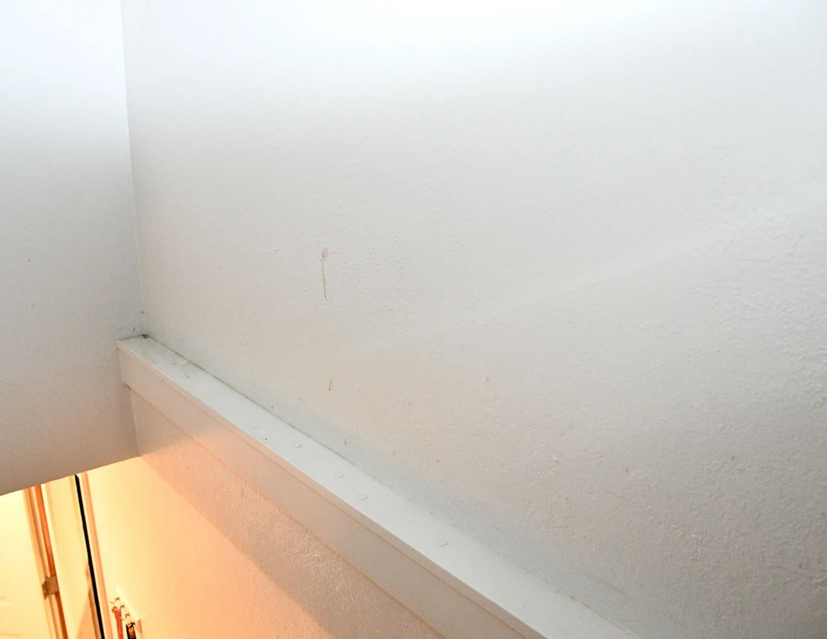 Pale stairwell wall with a faint vertical mark above horizontal white trim.
