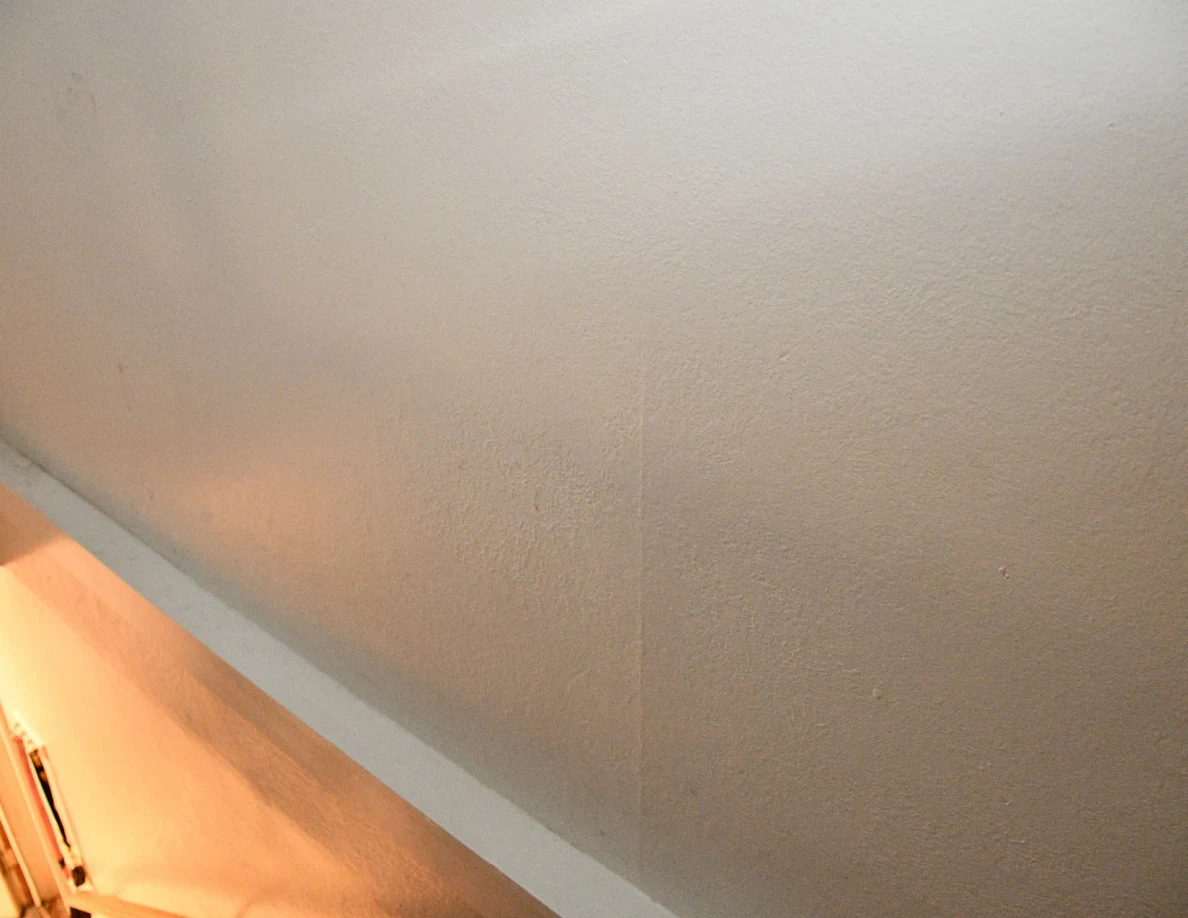 Pale stairwell wall with faint marks above white trim.