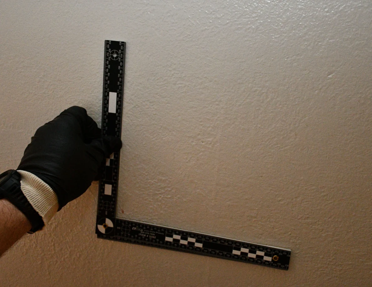 L-shaped ruler held beside a faint vertical mark on a pale textured wall.
