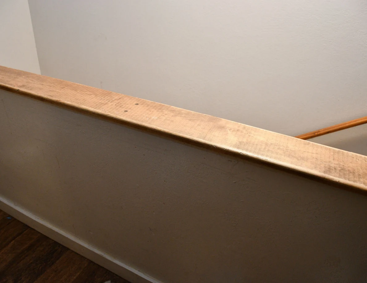 Wood-capped stair half-wall with pale wall surface and wood-look flooring.