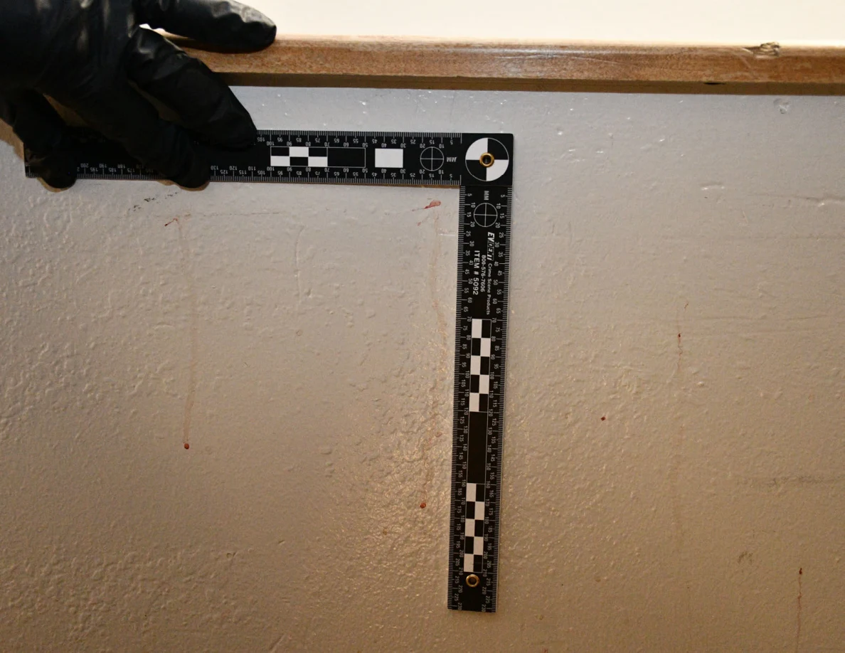 L-shaped measurement ruler held beside thin reddish streaks beneath a wooden half-wall cap.