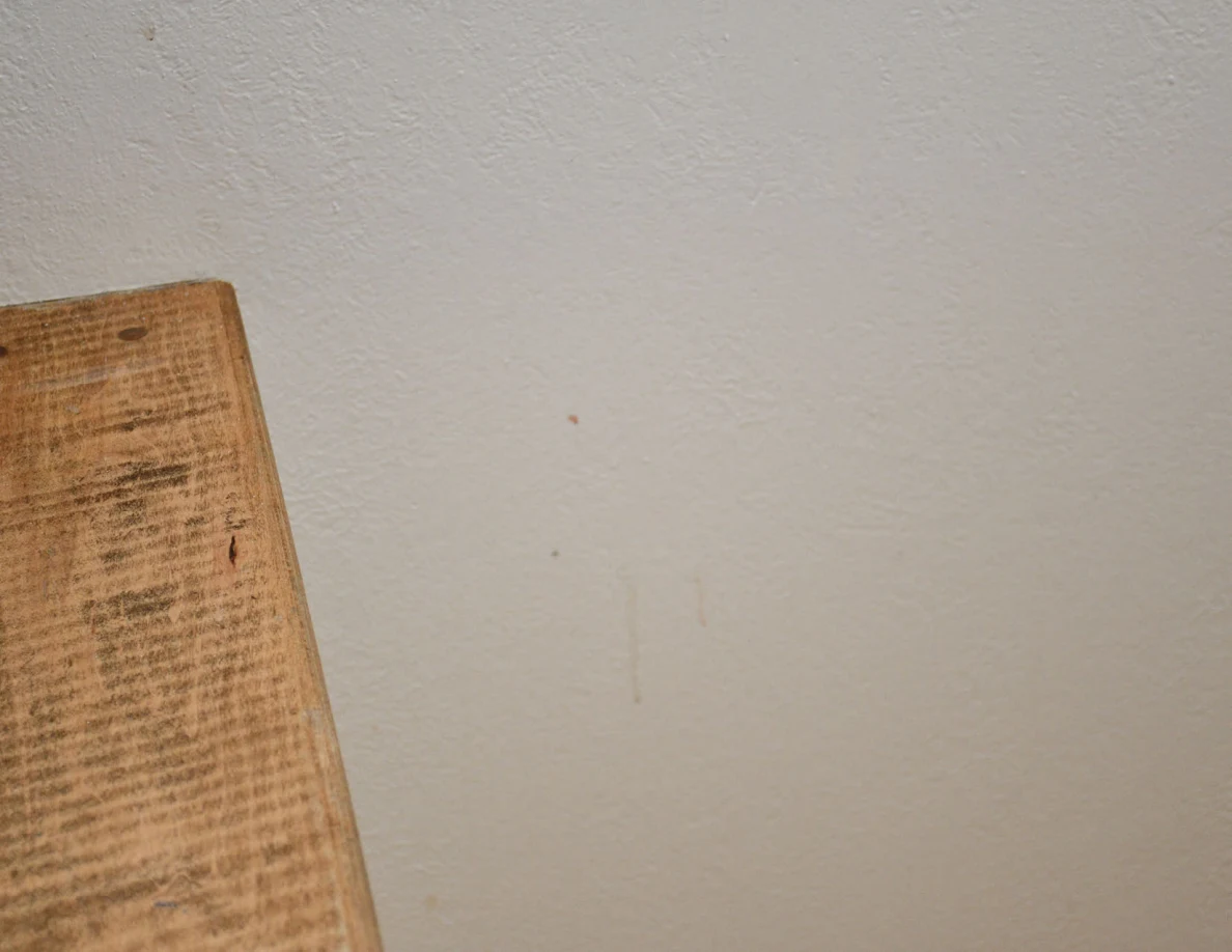 Closer view of faint marks on a pale stairwell wall beside a wooden cap.