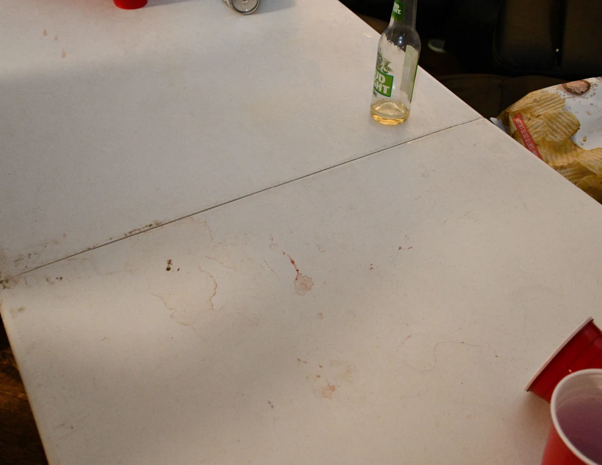 White folding table with faint reddish marks, a clear bottle and red plastic cups.