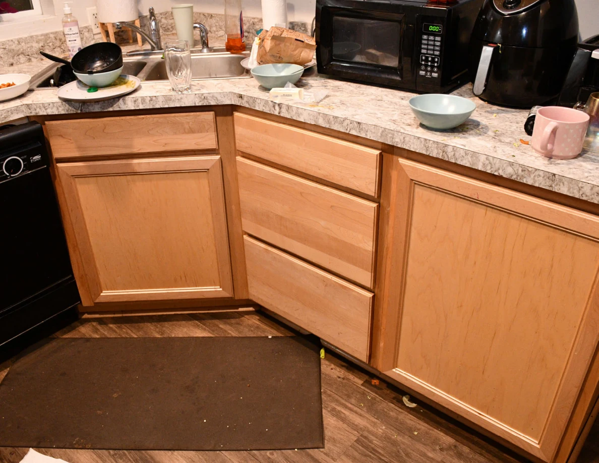 Kitchen counter and wooden cabinets with sink, bowls, pink mug, microwave and air fryer.