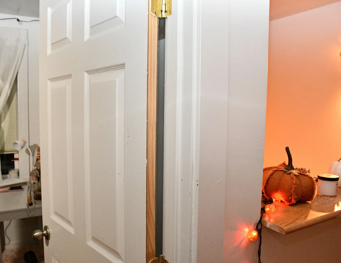 Partly open white panel door beside a stair landing with decorative pumpkin and orange lights.