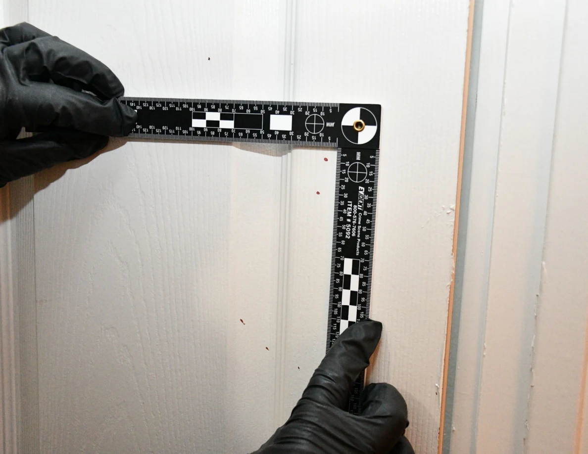 L-shaped ruler held beside small reddish spots on a white door panel.