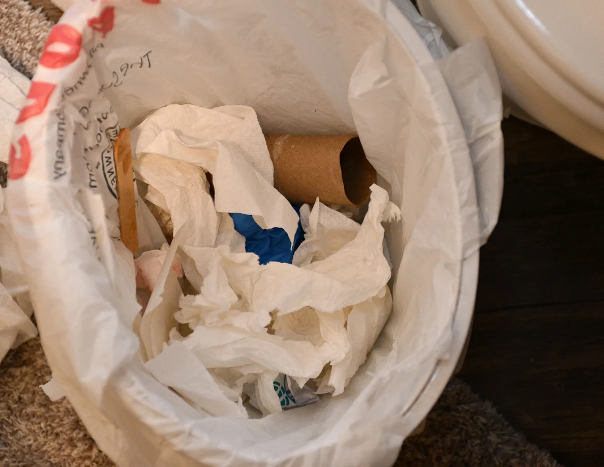 Close view inside a bathroom trash bin with tissues, cardboard roll and blue glove material.
