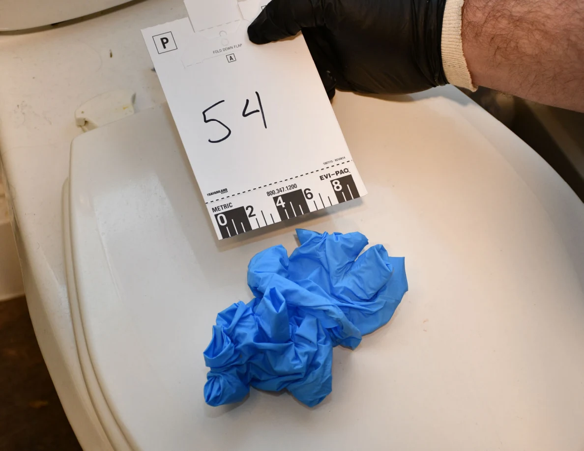 Blue disposable gloves on a white toilet lid beside card 54.