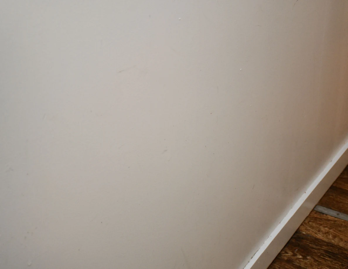 Closer view of faint scuffs and marks on a pale hallway wall.