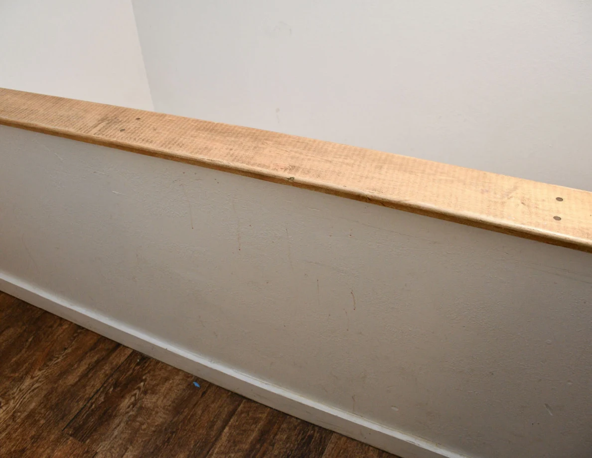 Wood-capped stair half-wall with faint vertical marks on its pale surface.