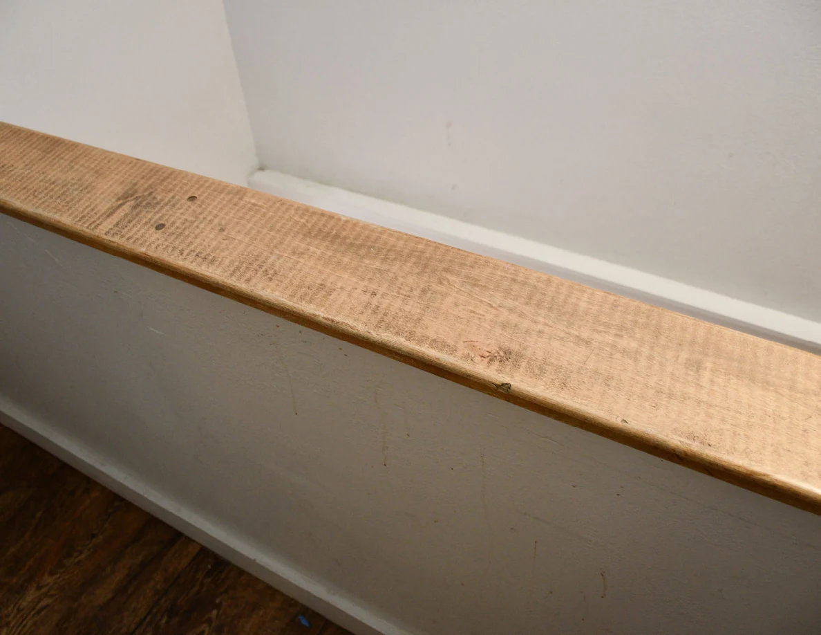 Angled view of a worn wooden half-wall cap and faint marks on the walls.