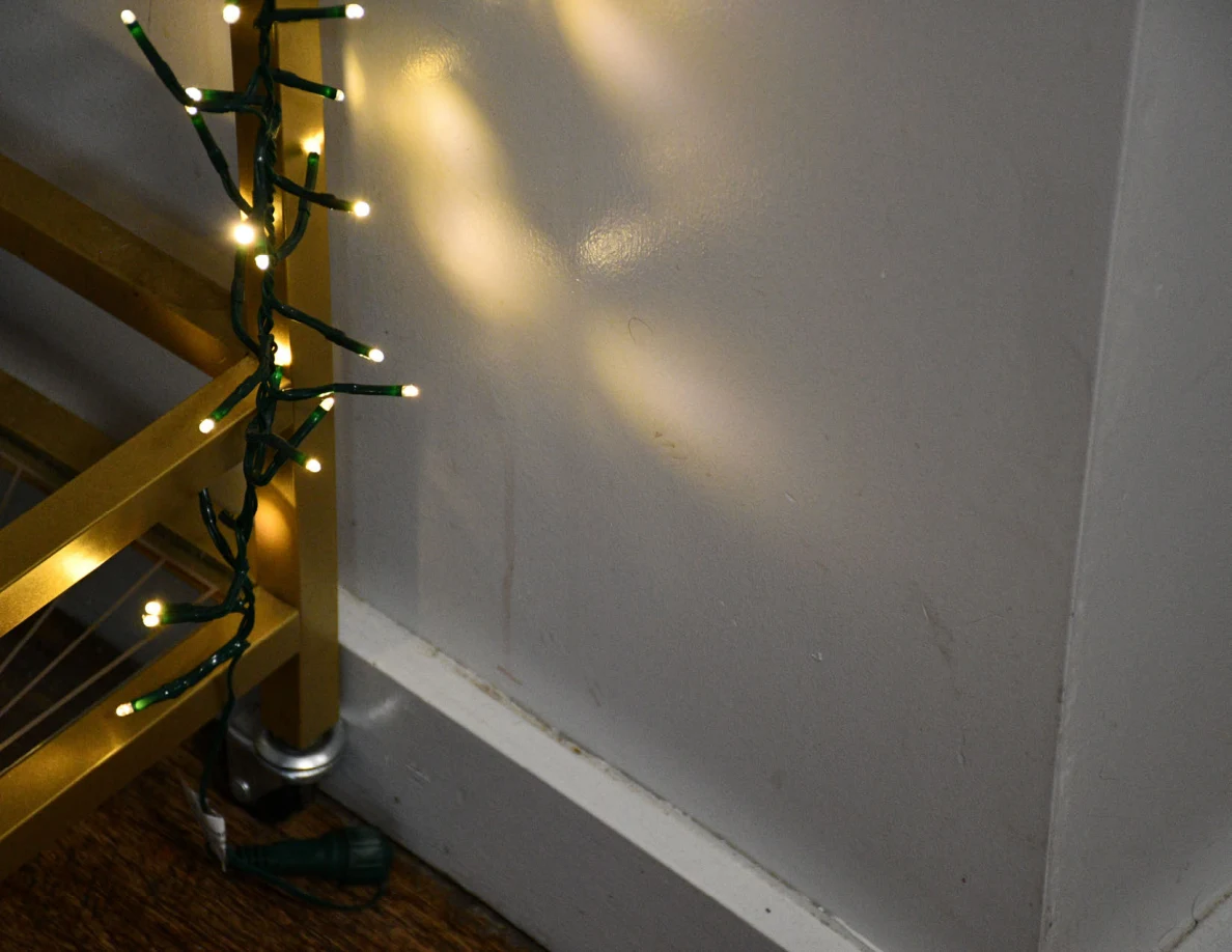 Close view of string lights wrapped around a gold cart beside a pale wall.