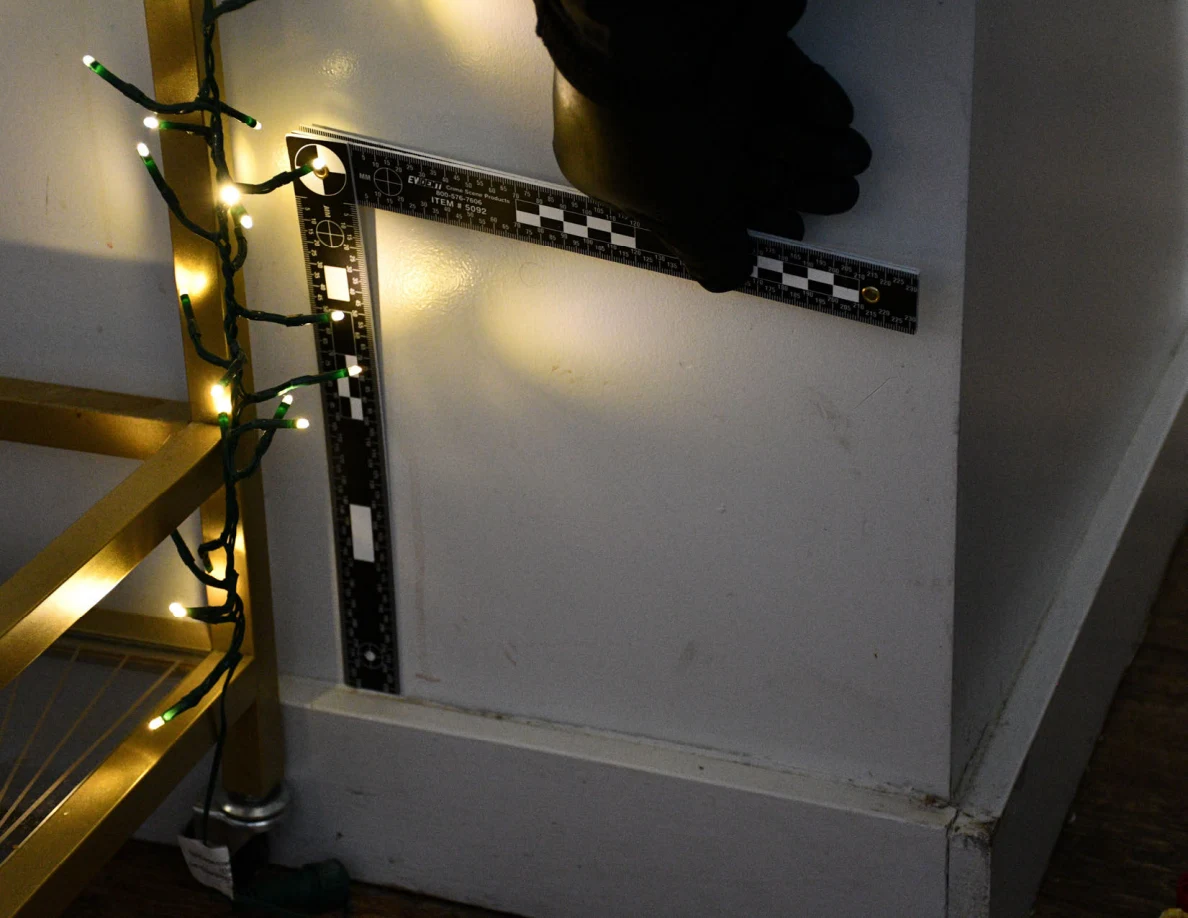 L-shaped ruler held against a pale wall beside a serving cart and string lights.
