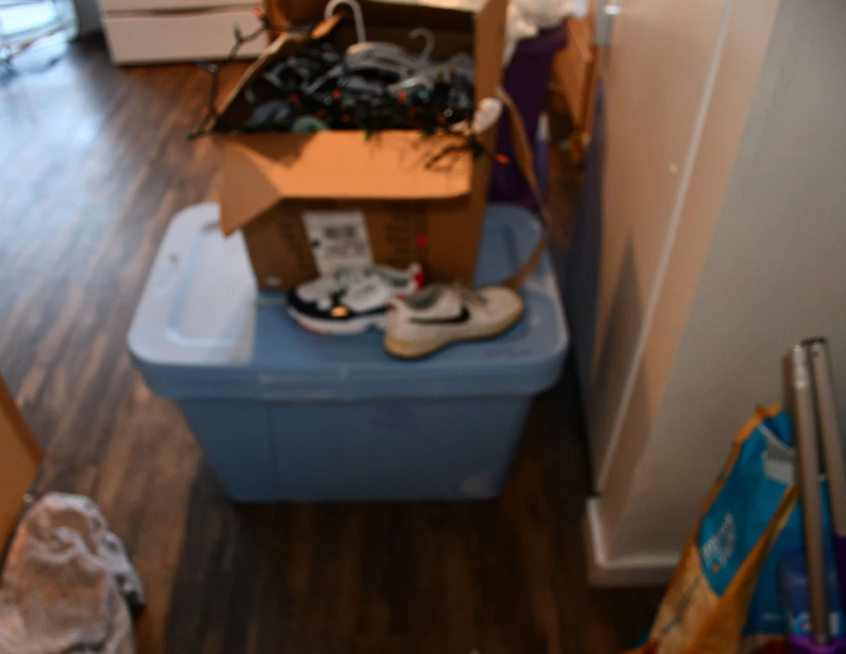 Blue storage tote with athletic shoes and a cardboard box stacked on its lid.