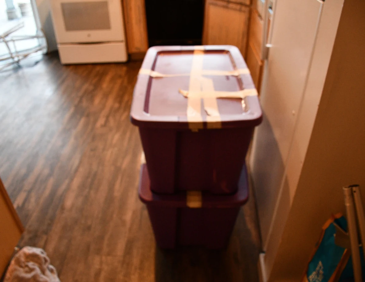 Two purple storage totes stacked near a kitchen, with tape across the upper lid.