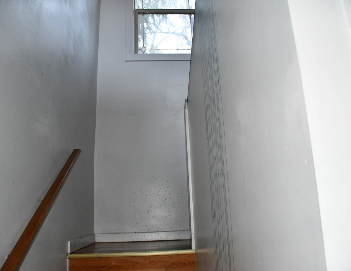Narrow stairwell with pale walls, wooden handrail and a high window.