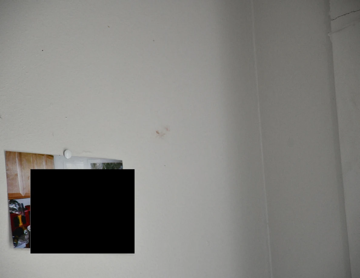 Pale wall with faint marks above a partly blacked-out pinned photograph.