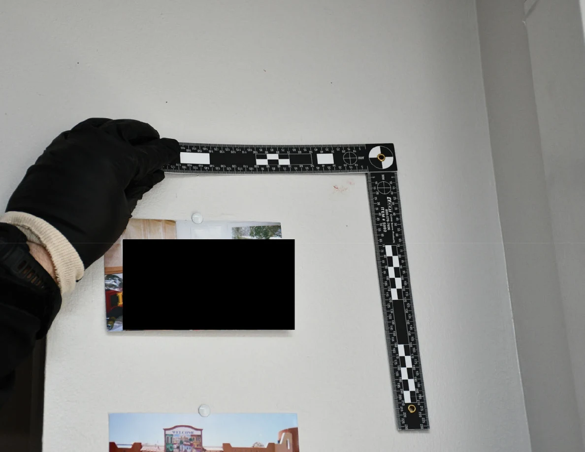 L-shaped ruler held on a pale wall above pinned photographs, one mostly blacked out.