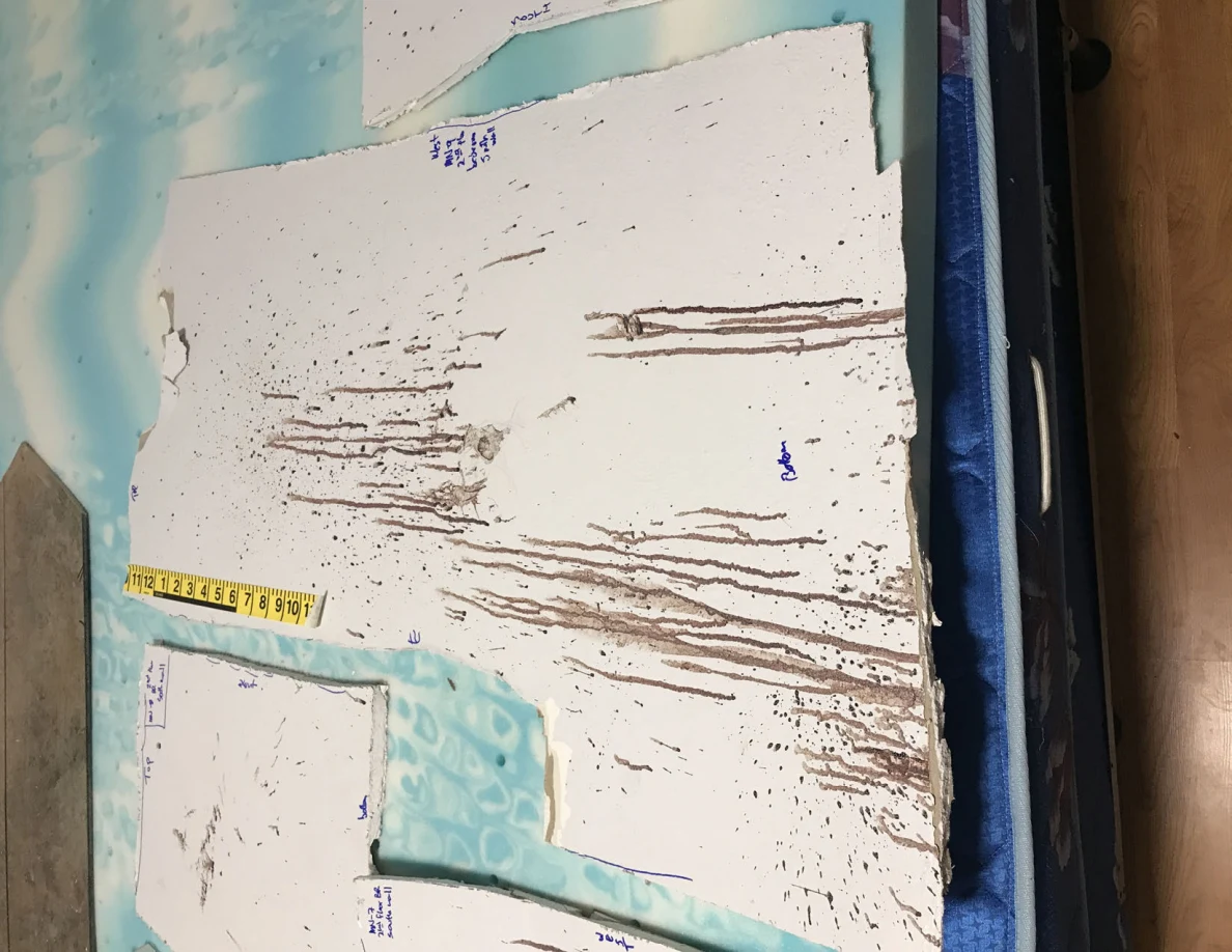 Large white wall-panel cutout with long dark streaks beside a yellow measurement scale.