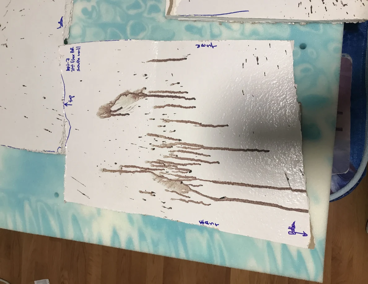 White panel section with dark streaks and handwritten edge labels on a blue patterned surface.
