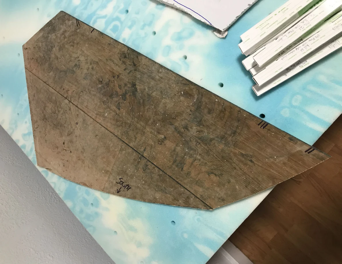 Wooden panel cutout with dark marks on a blue patterned surface beside white panel pieces and narrow boxes.