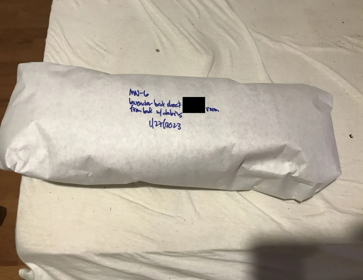 Long white-paper-wrapped package with blue handwriting and a small black redaction on a pale sheet.