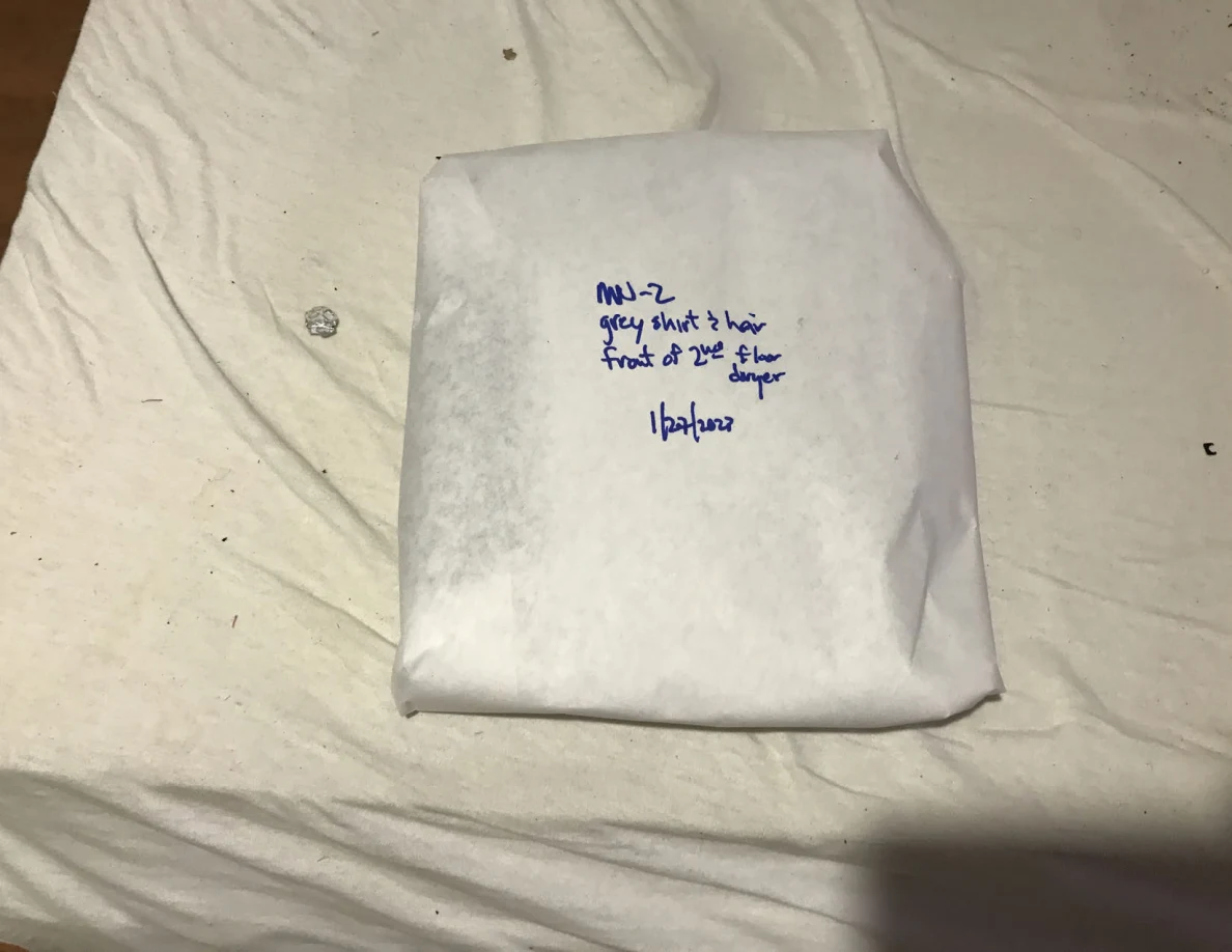 Square white-paper-wrapped package with handwritten label on a pale sheet.