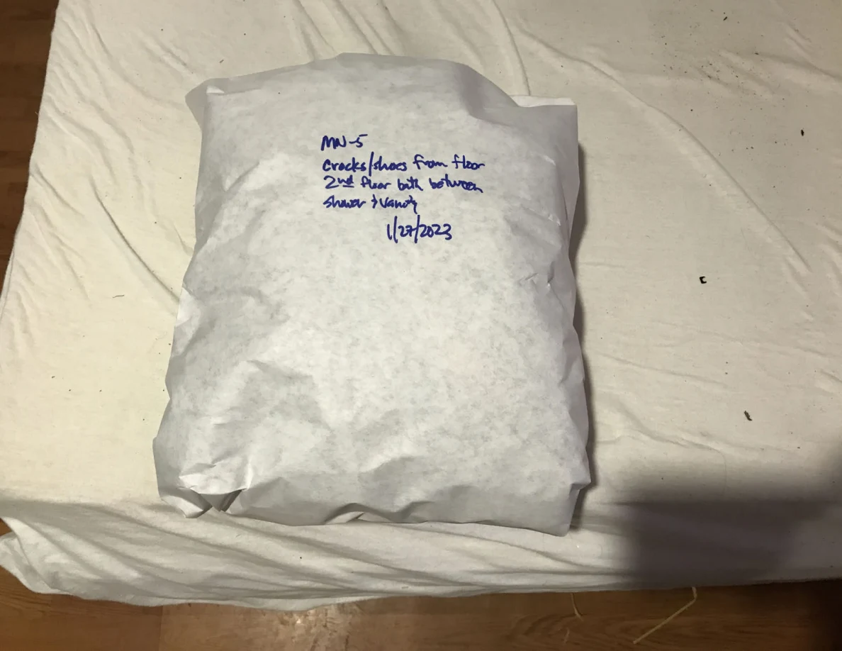 Rectangular white-paper-wrapped package with handwritten label on a pale sheet.