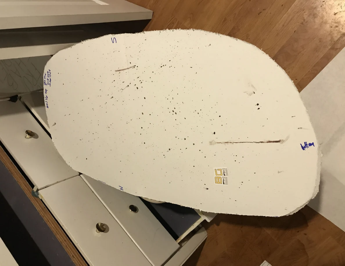 Rounded white panel cutout covered with dark specks and streaks, resting above open drawers.
