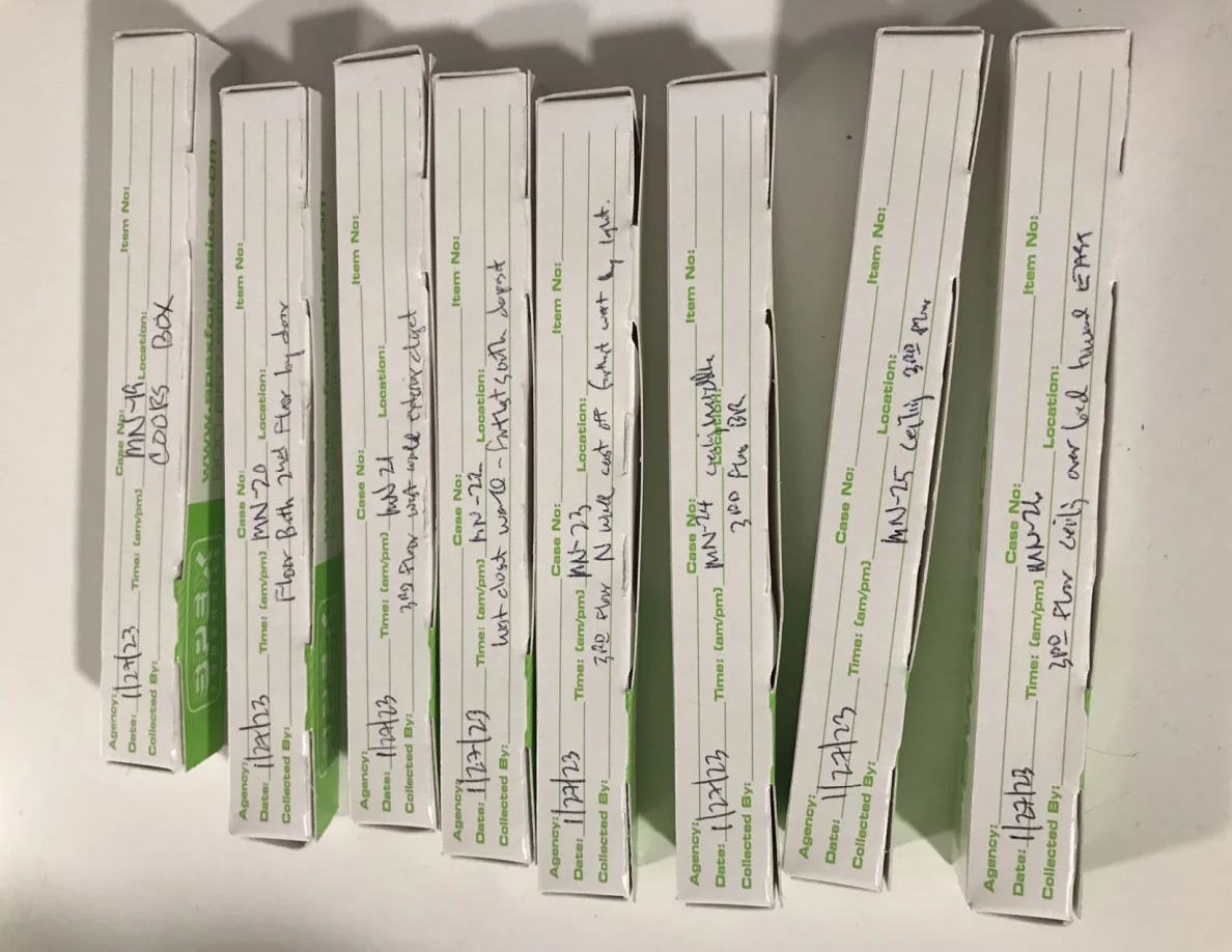 Row of narrow white sample boxes with green printing and handwritten labels.