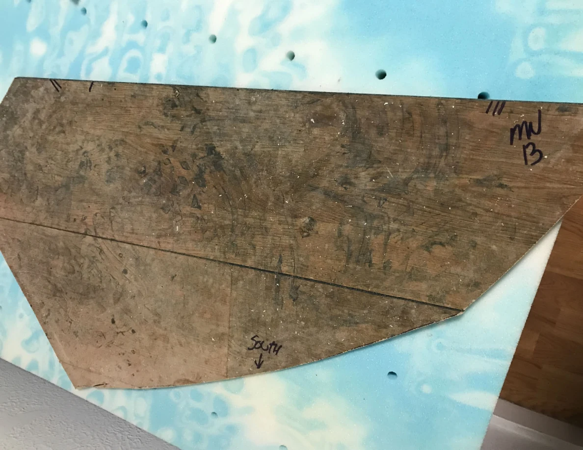 Wooden panel cutout with dark marks and handwritten labels on a blue patterned surface.