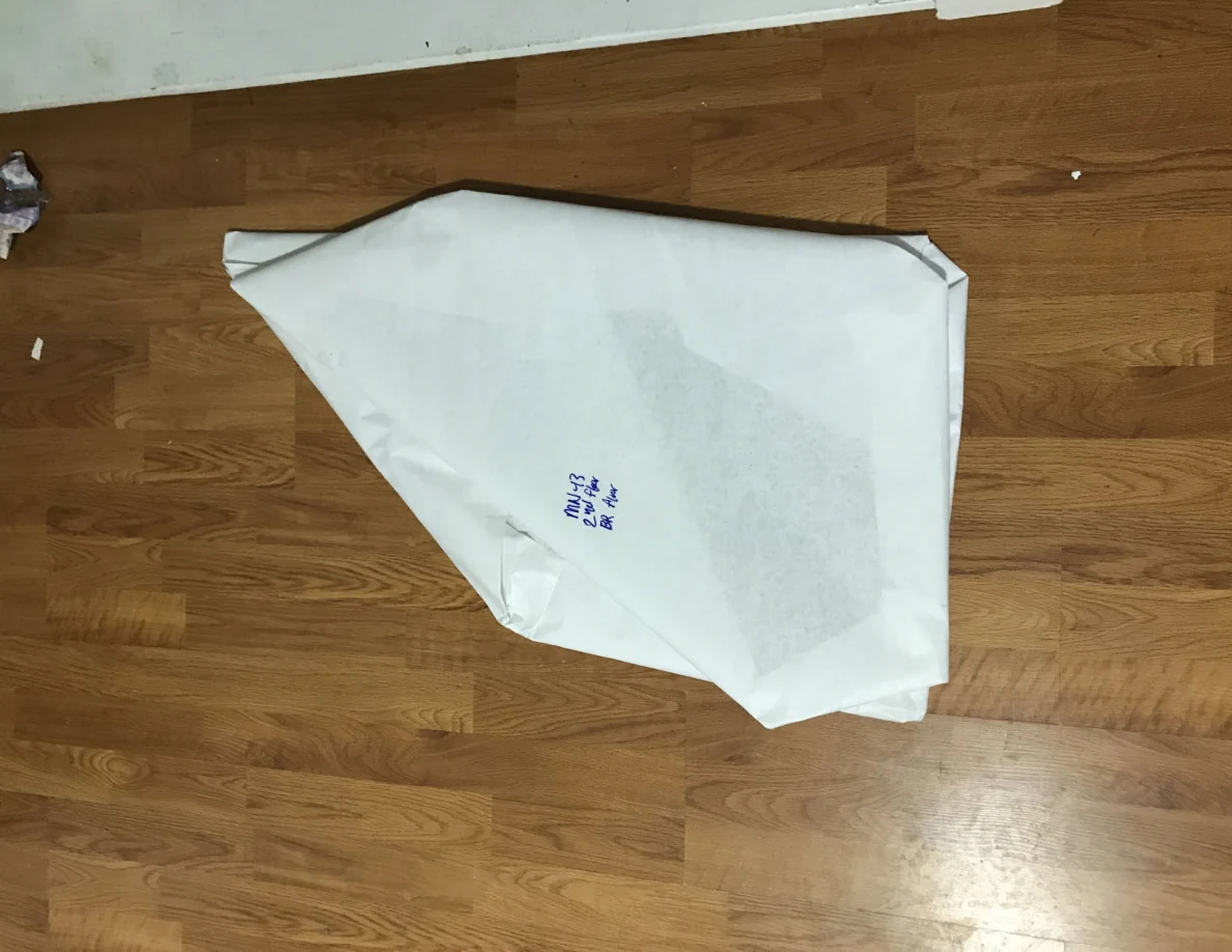 Broad angular white-paper-wrapped panel with handwritten label on a wooden floor.