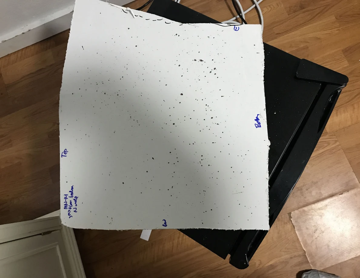 Rectangular white panel cutout with scattered dark spots and handwritten edge labels.