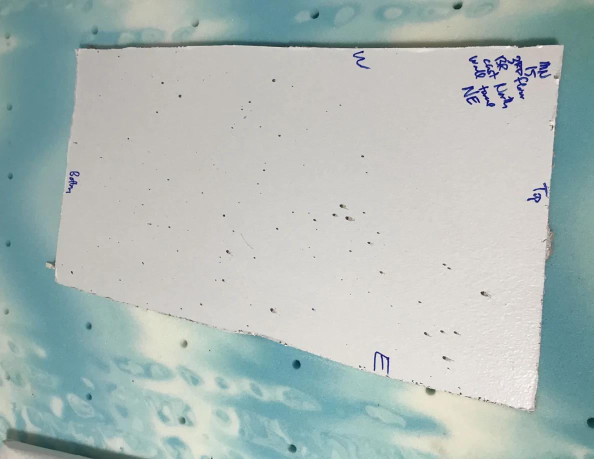 White rectangular panel with dark specks and handwritten orientation labels on a blue surface.