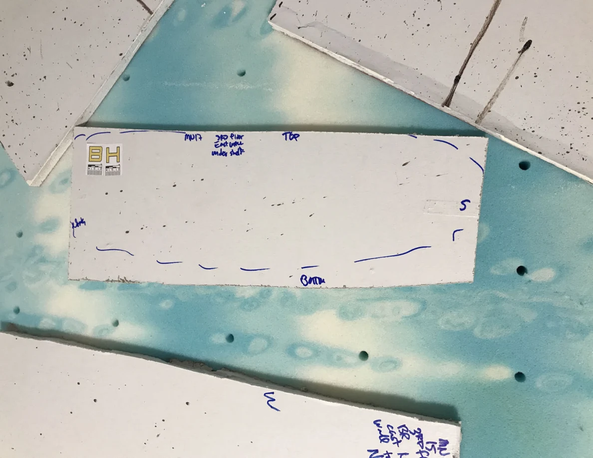Narrow white panel cutout with small dark spots and blue handwritten edge markings.