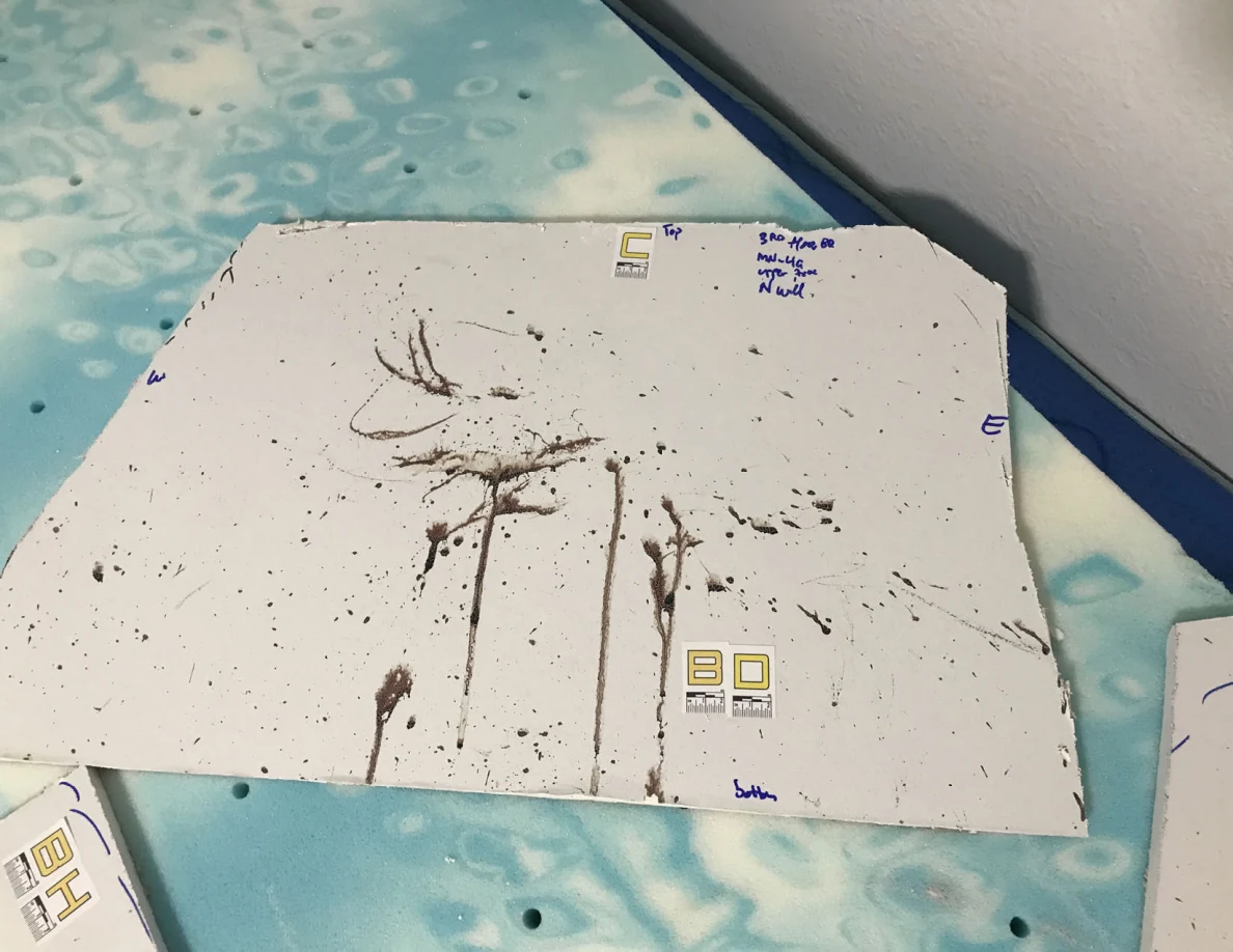 White panel cutout with concentrated dark streaks and specks on a blue patterned surface.