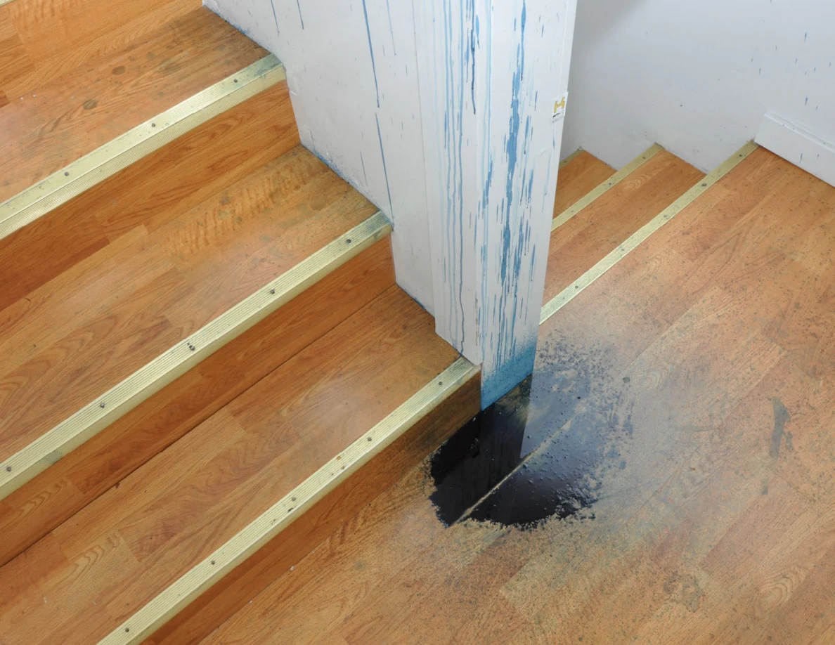 Stair landing with blue streaks on a half-wall and a dark blue patch on the wooden floor.