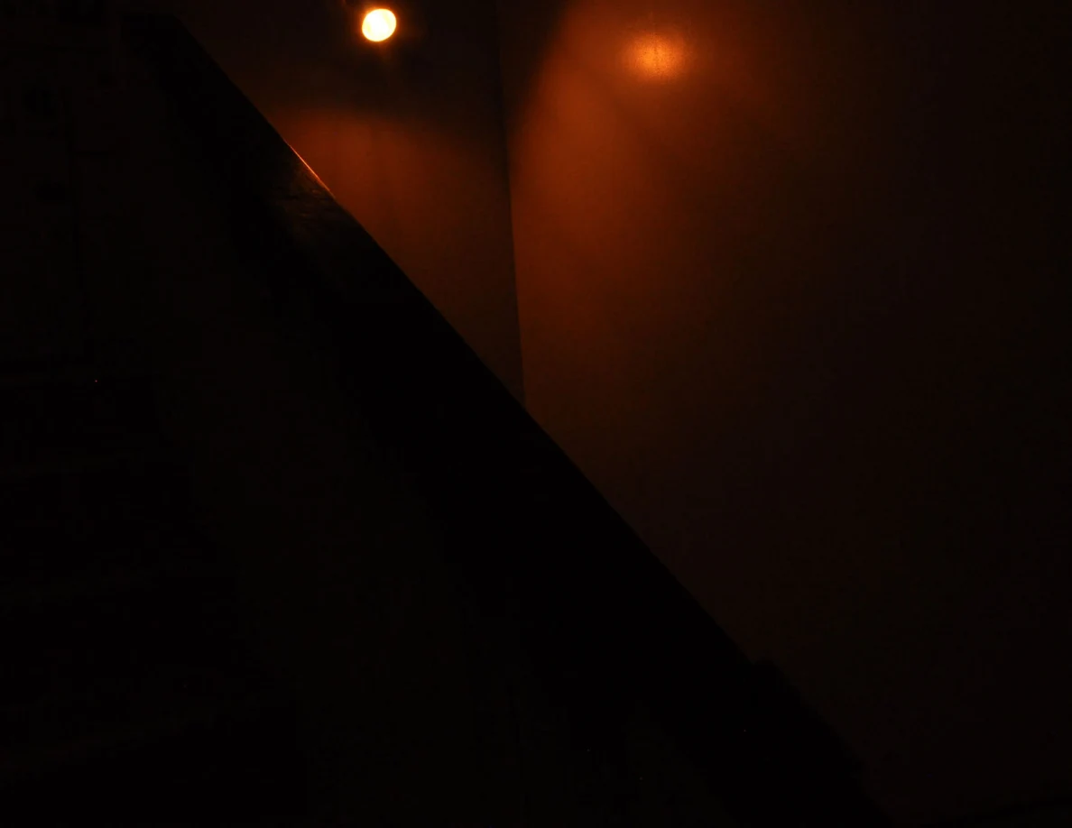Dim stairwell view with a warm wall light and a dark half-wall cap.