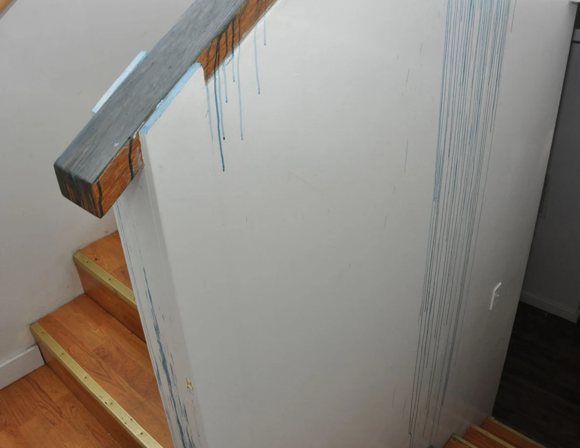 Long blue streaks running down a pale half-wall beside wooden stairs.
