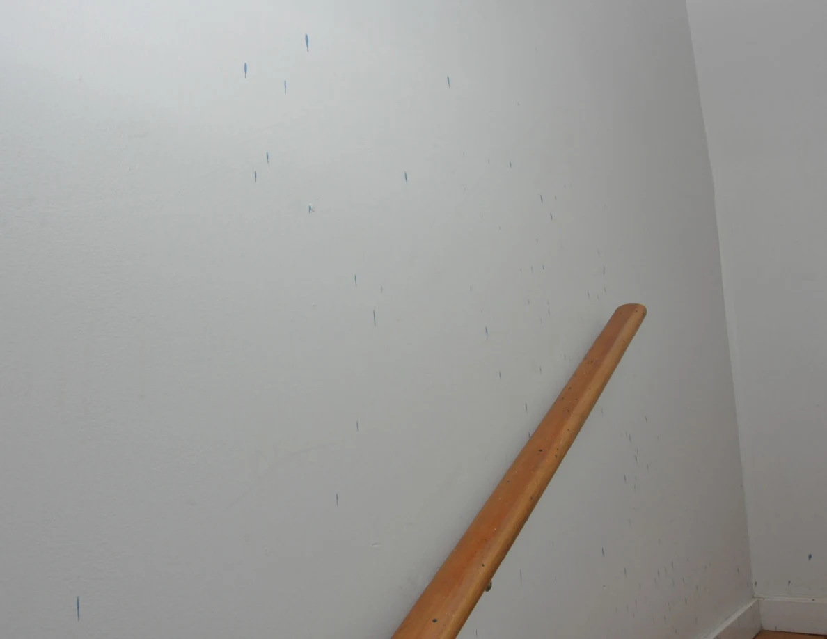 Small blue streaks on a pale stairwell wall above a wooden handrail.