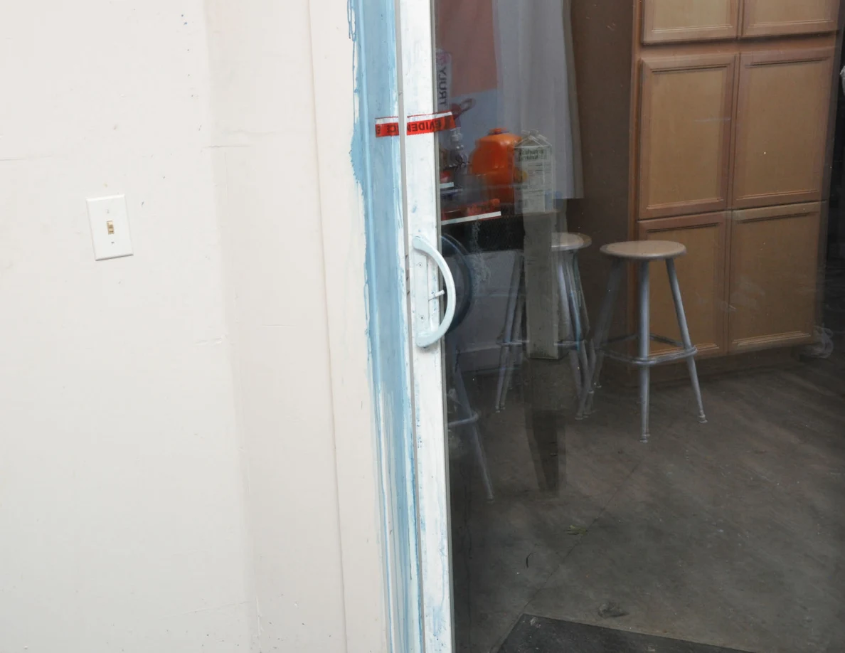 Sliding glass door frame with blue marks and red evidence tape, with kitchen stools beyond.