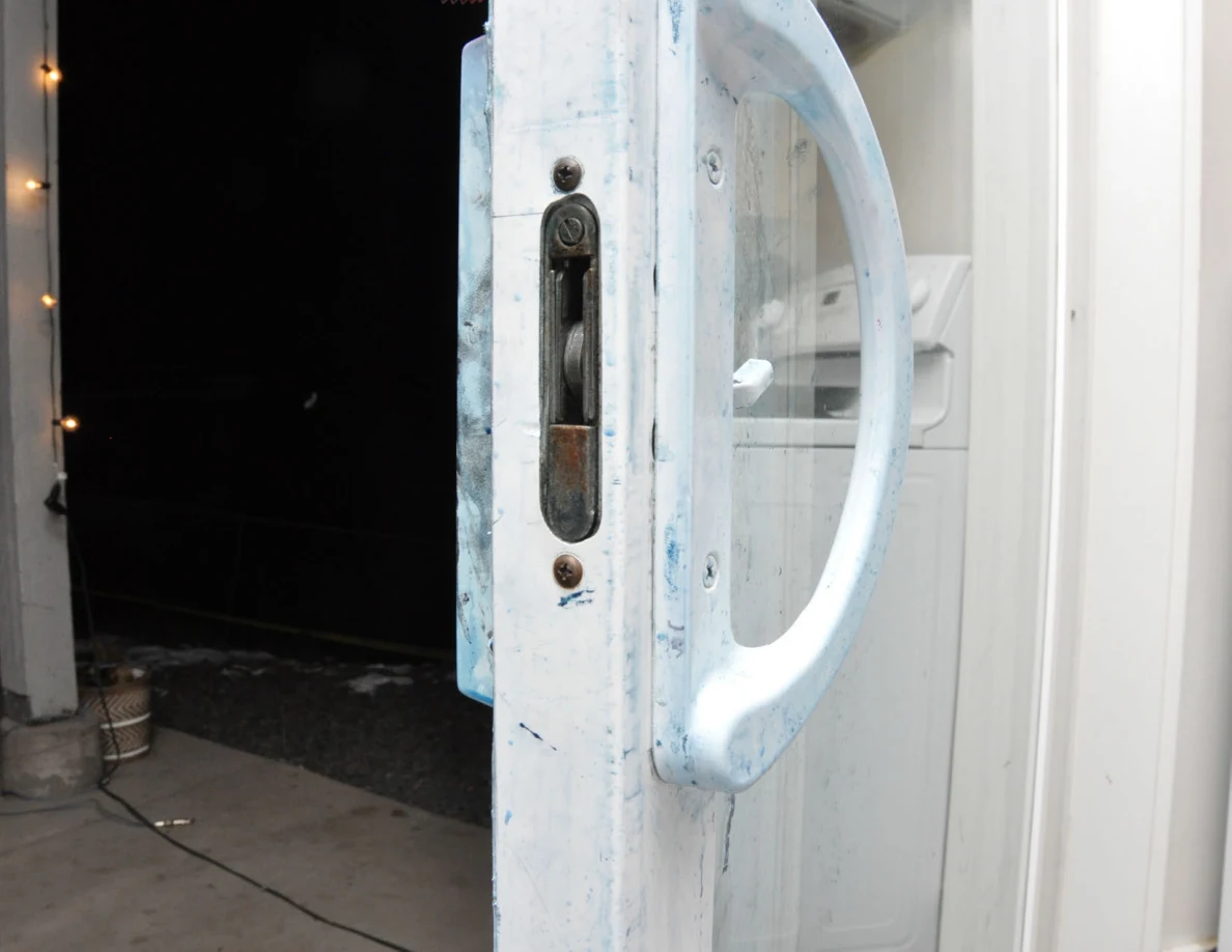 Sliding-door edge and latch opening beside a curved white handle with blue marks.