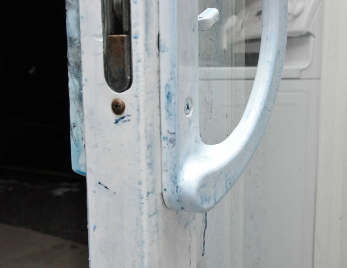 Closer view of a sliding-door handle, latch opening and blue marks on white frame.
