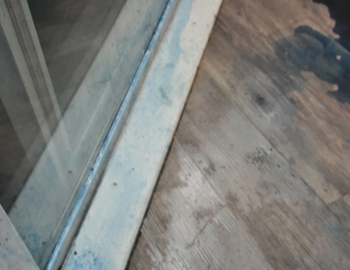 Sliding-door track and wood-look flooring with blue residue and a dark patch nearby.